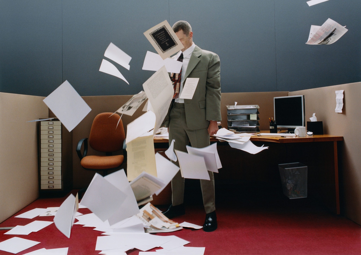 A man stands in an office, with papers flying all around him